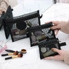 A hand holds a black mesh cosmetic storage pouch filled with makeup brushes and small beauty tools on a white marble surface.