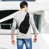 A man wearing a gray long-sleeve shirt and jeans is shown from the back, carrying a black tactical sling backpack.