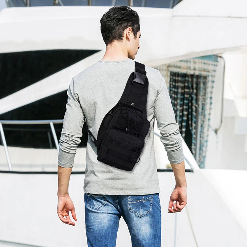 A man wearing a gray long-sleeve shirt and jeans is shown from the back, carrying a black tactical sling backpack.