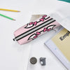 Pink leather pencil case with black stripes and pink bows resting on a white surface.