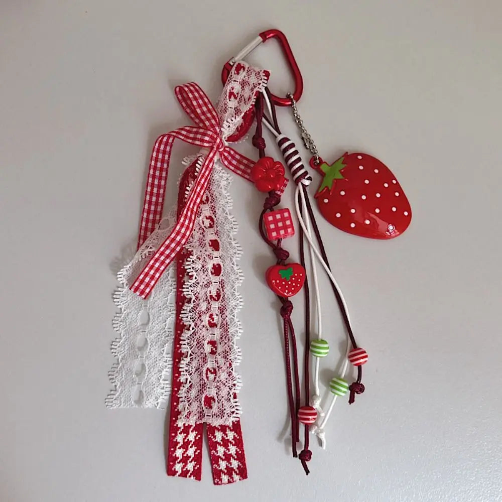 A red and white lace ribbon charm featuring a strawberry shape and various bead accents.