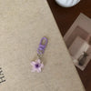 A purple resin flower keychain attached to a silver ring, resting on a beige surface.