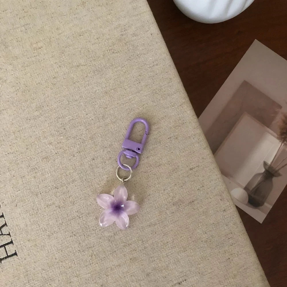 A purple resin flower keychain attached to a silver ring, resting on a beige surface.