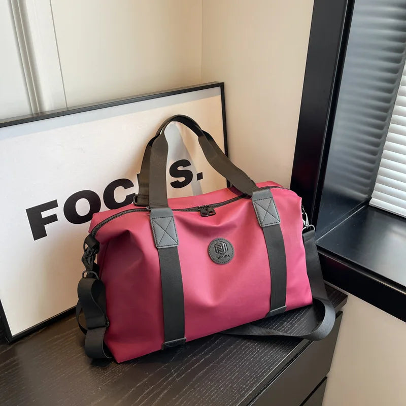 A pink and black Oxford cloth travel tote bag is displayed on a dark surface next to a black cabinet.
