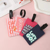Pink and dark blue silicone letter luggage tags with black straps resting on a light pink surface.