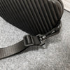 A black pleated PU leather shoulder bag with a black strap resting on a gray carpet.