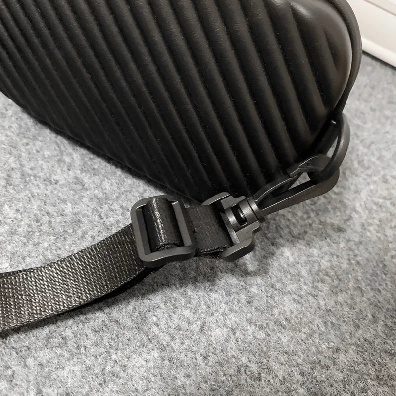 A black pleated PU leather shoulder bag with a black strap resting on a gray carpet.