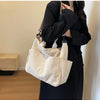 A woman holds a cream colored corduroy multi-pocket tote bag against a black coat.