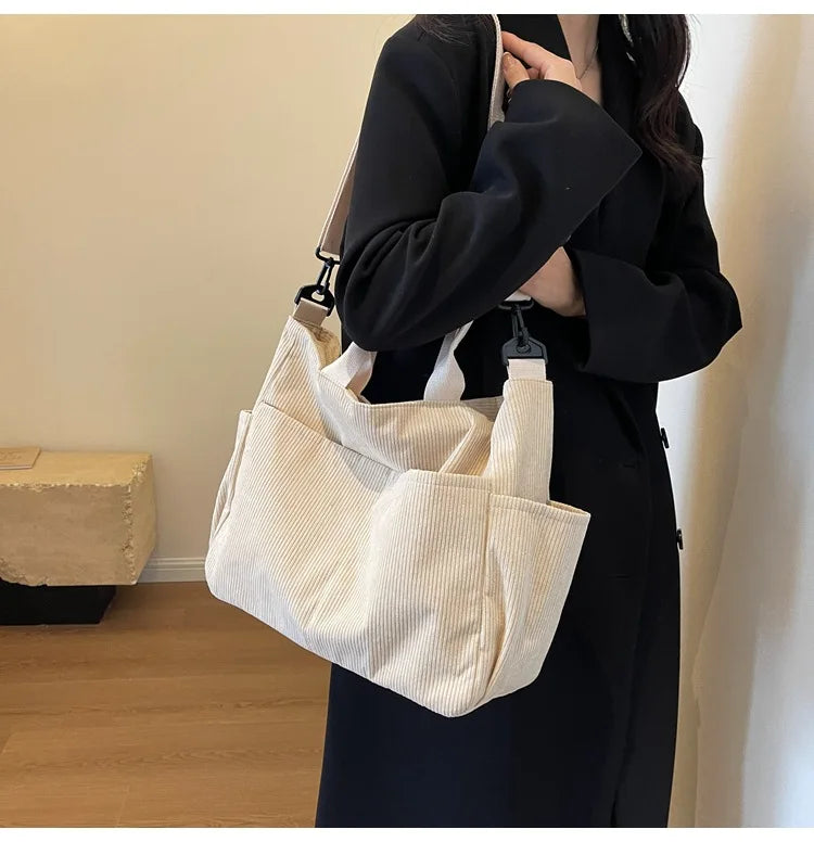 A woman holds a cream colored corduroy multi-pocket tote bag against a black coat.