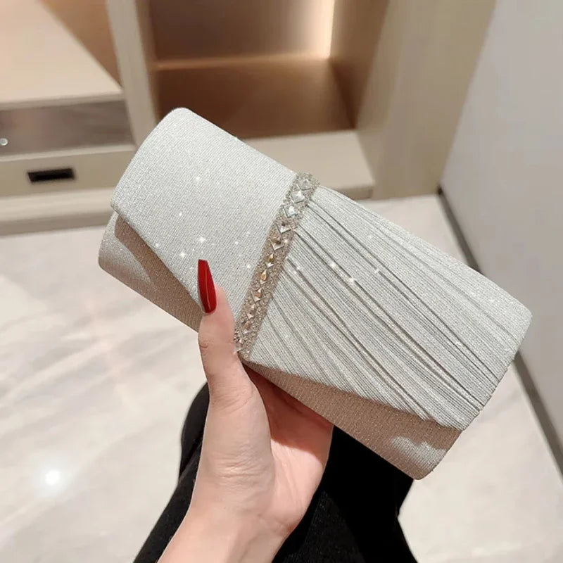 Eine Hand hält eine elegante silberne Halskette als Schultertasche mit strukturiertem Silberstoff und funkelnden Verzierungen