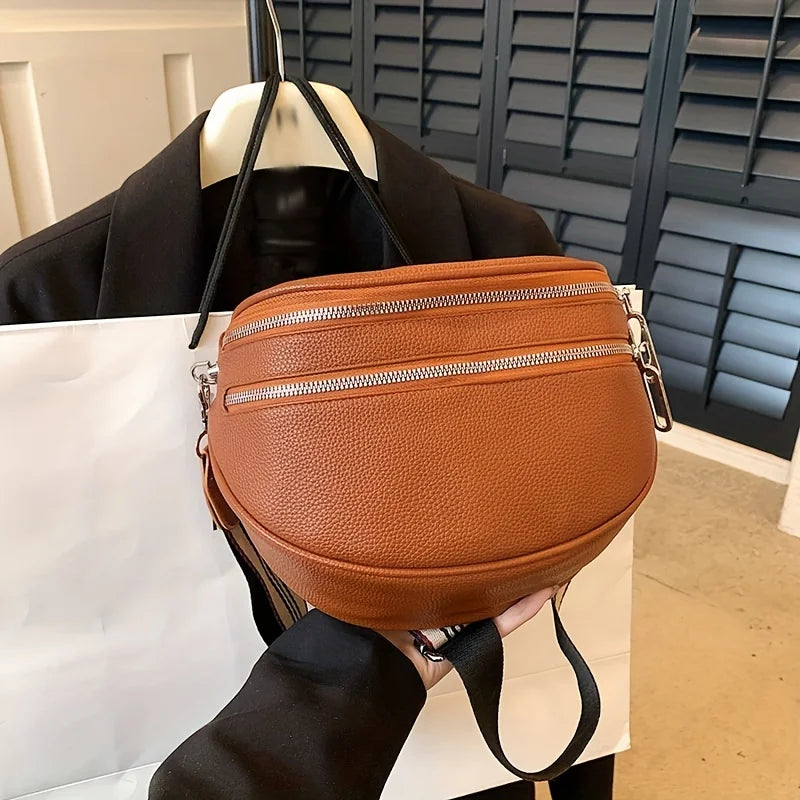 A brown soft leather crossbody bag with double zippers is displayed on a white box.