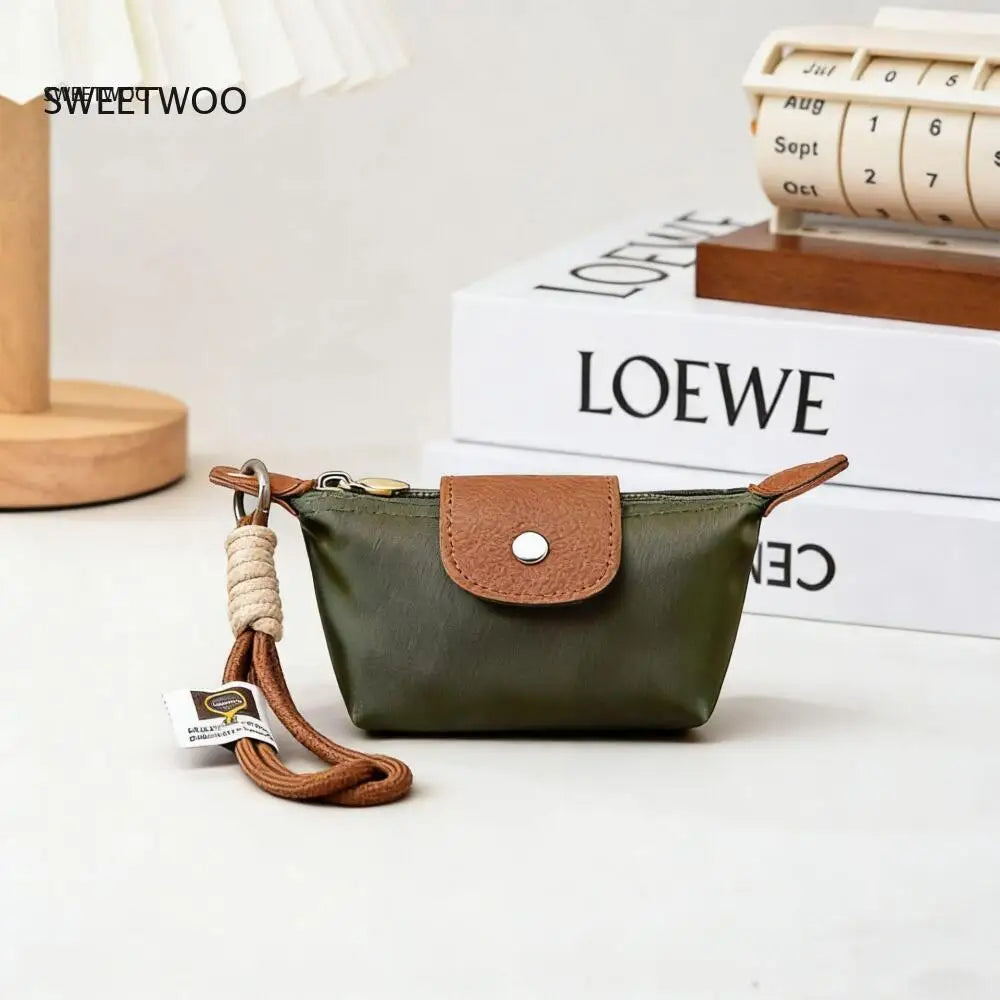 A dark olive green compact coin purse with a brown leather flap and keychain strap resting on a white surface.