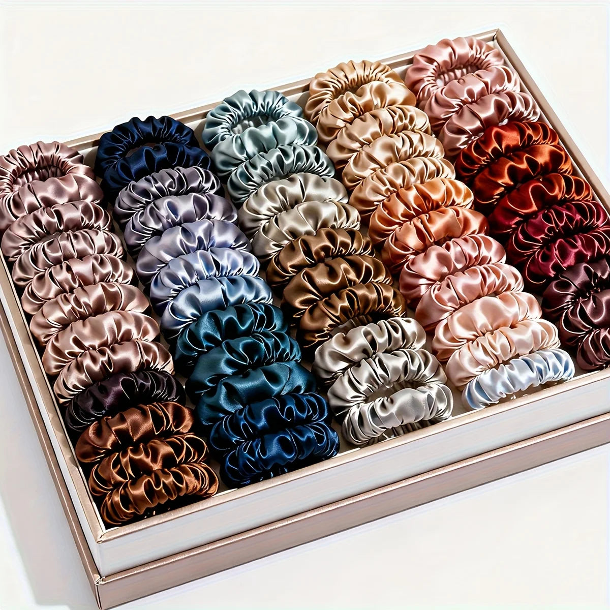 A box filled with 19 pieces of thin scrunchies hair ties in a variety of mixed satin colors.