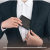 A hand is holding a black carbon fiber microfiber wallet inside a white dress shirt and dark suit jacket.