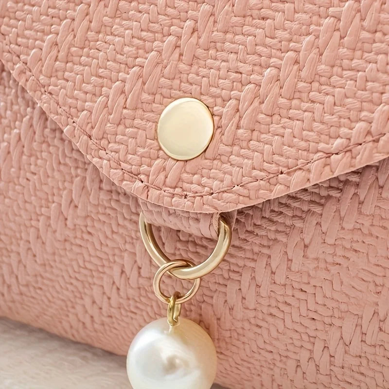 A close-up of a dusty rose woven texture fabric on a crossbody bag featuring a gold-toned button and a pearl charm.