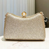 A gold glitter clutch bag with a pearl embellishment and rhinestone detailing resting on a white surface.