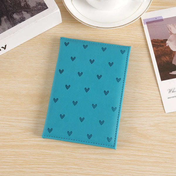 A teal leather passport cover featuring a repeating pattern of small blue hearts, placed on a light wooden surface.