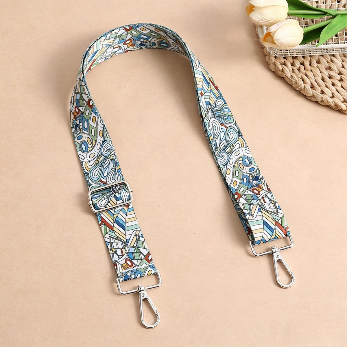 A patterned nylon crossbody bag strap with metal buckles lying on a beige surface.