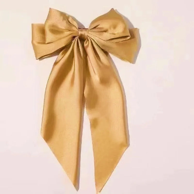 A golden silk bow hair clip tied in a large bow shape.