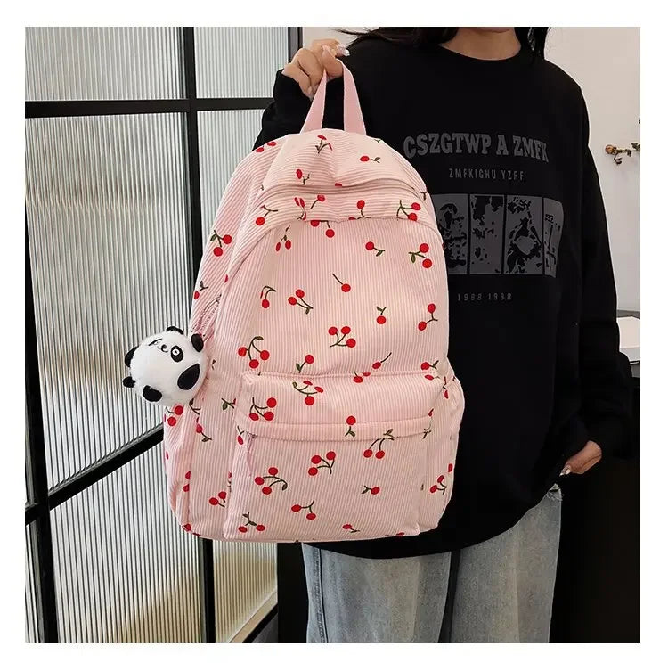 A pink corduroy fashion backpack with a patterned fabric and a white panda charm is worn by a person.