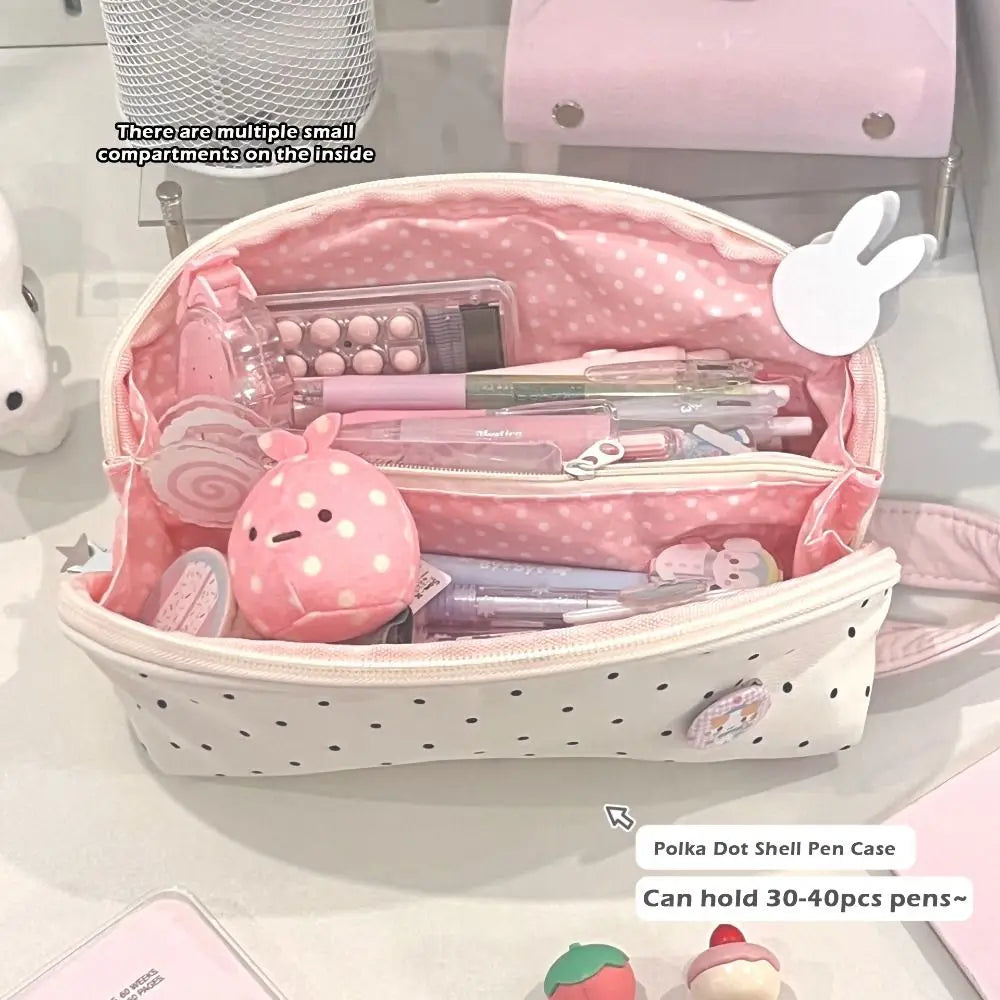 A pink polka dot shell pencil case is open, showing multiple small compartments and various pens inside.