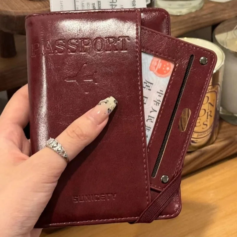 A hand holds a maroon leather passport wallet with RFID blocking features and a card slot.