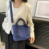 A woman wearing a cream-colored blouse and dark skirt holds a navy blue canvas crossbody bag.