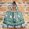 A reusable shopping bag featuring a green and white patterned fabric with elephant motifs, displayed against a brick wall.