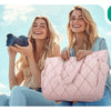 Two young women smiling while holding a pink quilted puffy tote bag outdoors with a cityscape in the background.