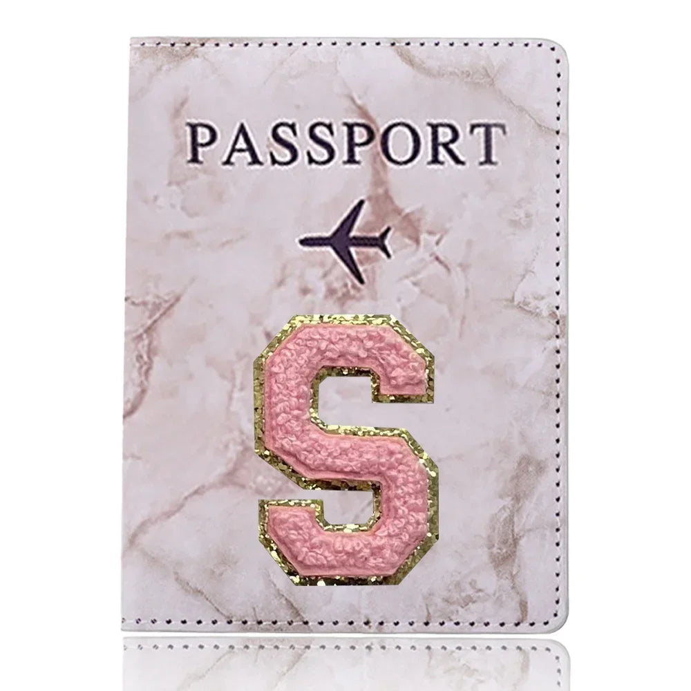 Carátula de pasaporte de mármol rosa con una S dorada grabada y un icono de avión negro.