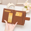 A hand holds a brown RFID-blocking compact bifold zipper wallet with gold cards and a white alarm clock in the background.