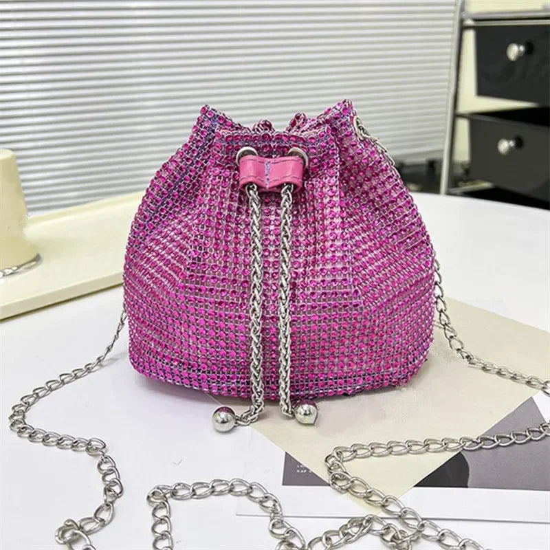 Bolso cruz con cordón de strass magenta y cadena plateada sobre superficie blanca.