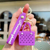 A purple silicone heart beach bag keychain is held in a hand against a blurred outdoor background.