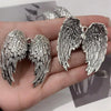 Silver metal angel wing keychain charm displayed on a hand.