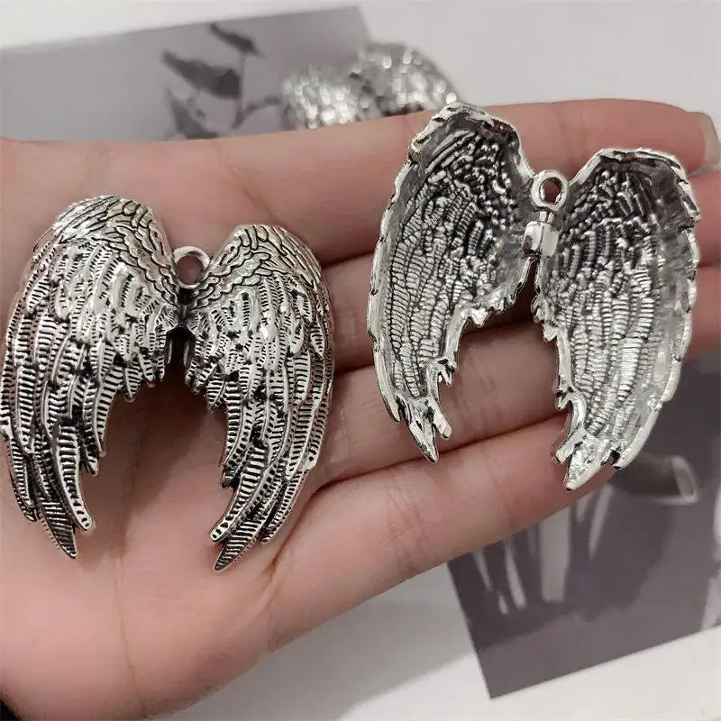 Silver metal angel wing keychain charm displayed on a hand.