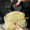 A yellow quilted puffer makeup bag being held above a black camera.