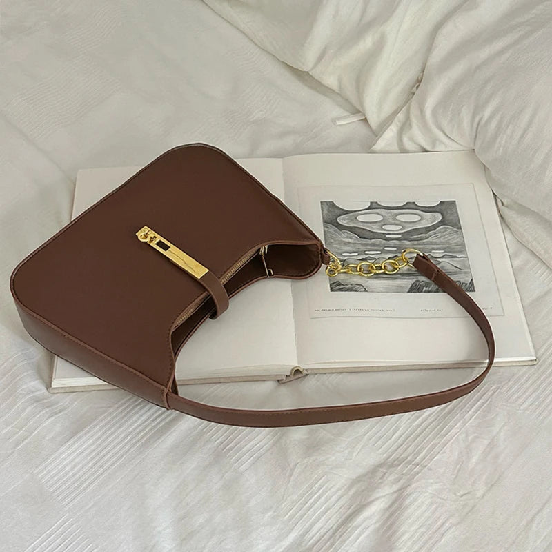 A brown PU leather hobo shoulder bag with a gold chain strap resting on an open book.