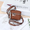 A brown leather coin purse with a zipper and silver chain is displayed on a map next to a minimalist book.