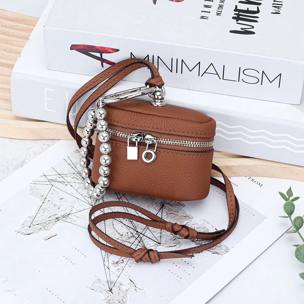 A brown leather coin purse with a zipper and silver chain is displayed on a map next to a minimalist book.