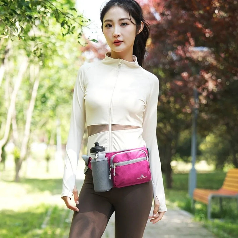 A woman wearing a white long-sleeved top and brown pants holds a pink waterproof invisible waist pack outdoors.