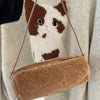 A small brown faux fur cylinder shoulder bag with a gold zipper is being held by a cat.