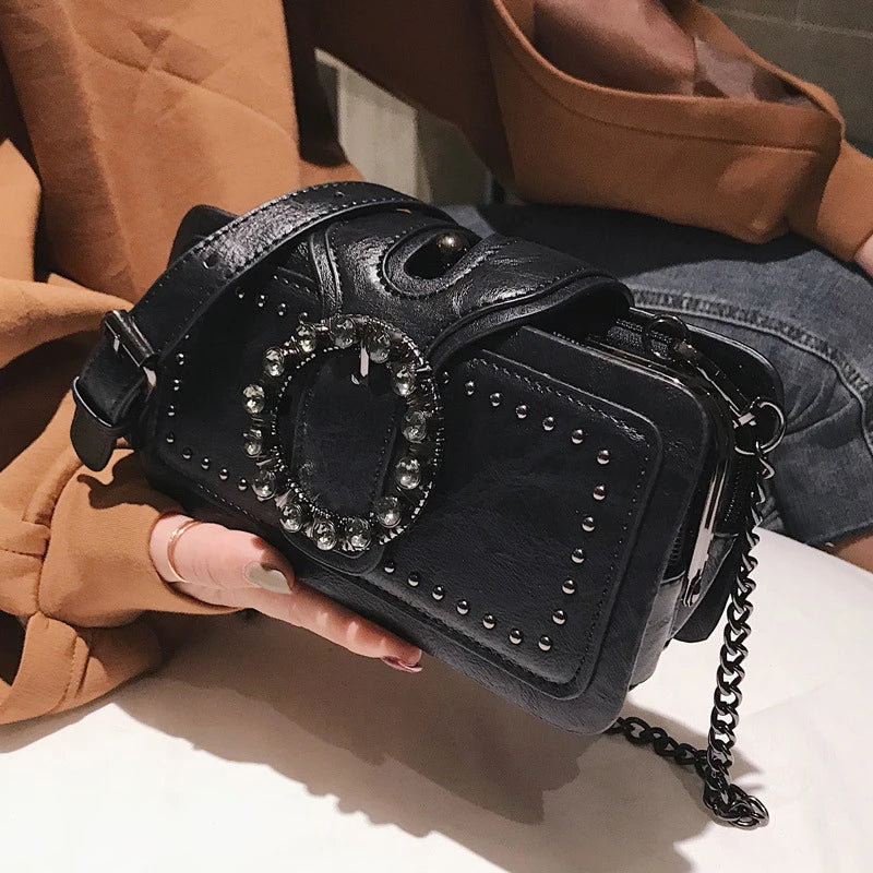 A black vintage PU leather crossbody bag with a rhinestone buckle resting on a white surface.