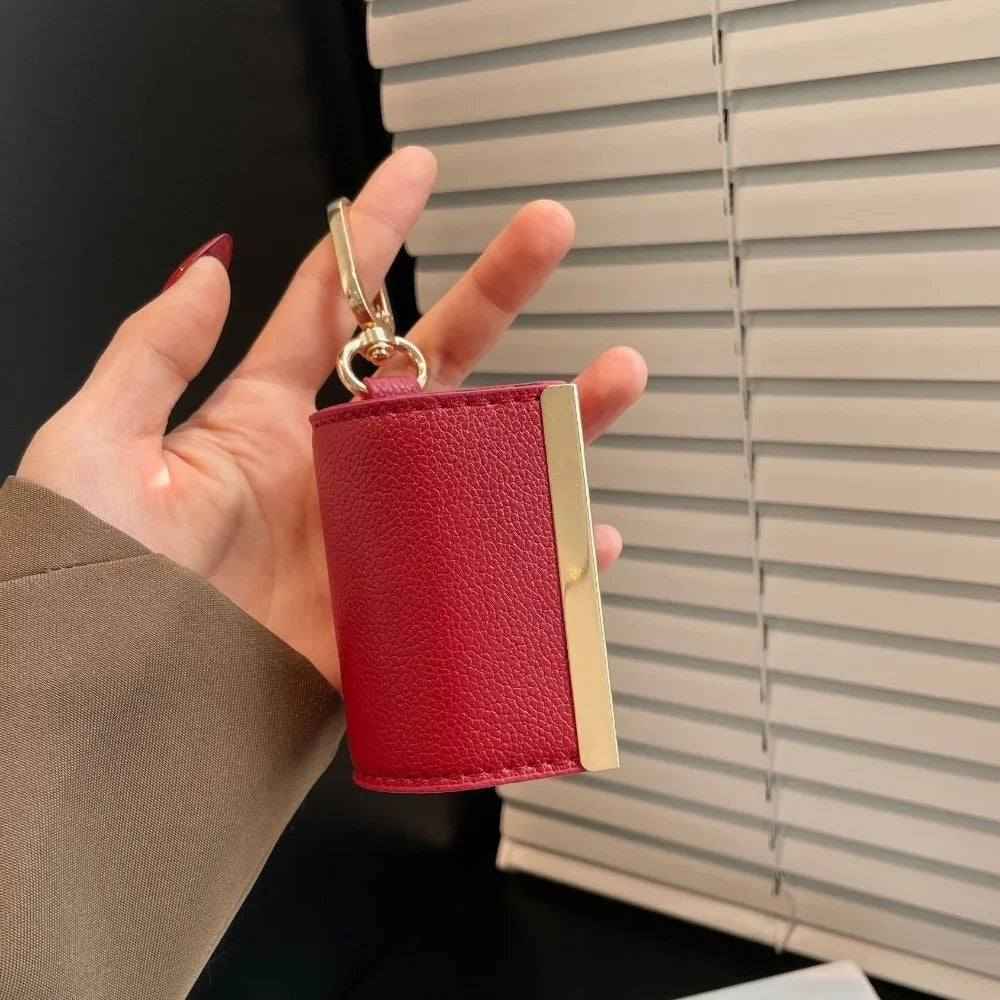 A hand holds a red nylon mini keychain tote bag with a gold clasp against a light gray slatted blind.