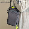 A dark gray adjustable water bottle carrier bag with a zippered pocket is shown hanging from a light-colored coat.