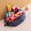 A dark blue foldable nylon storage bag filled with various food items including apples, eggs, jars, and packaged goods.