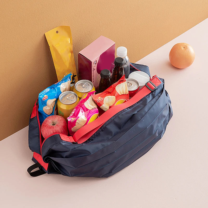 A dark blue foldable nylon storage bag filled with various food items including apples, eggs, jars, and packaged goods.