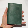 A dark green genuine leather passport holder with embossed eagle design and United States of America text being held in a han