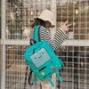 A person wearing a straw hat and striped shirt carries a bright teal robot backpack in front of a glass grid.