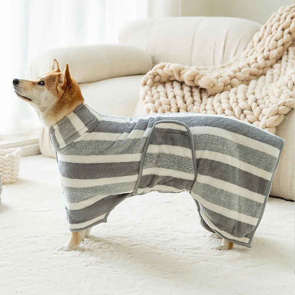 Un chien portant un peignoir de bain à rayures grises et blanches sur un tapis blanc à côté d'un canapé.