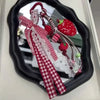 A red and white patterned strawberry bag charm keychain displayed in a black oval mirror frame.